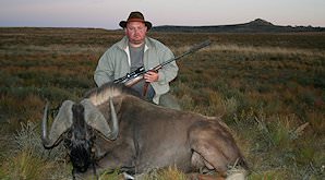 A hunter kneels behind his black wildebeest trophy.
