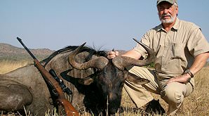 A hunter crouches alongside his blue wildebeest trophy.