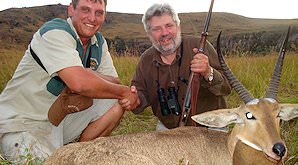 A hunter shakes hands with his professional hunter alongside their reedbuck trophy.