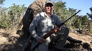 A hunter sits on the back legs of his elephant trophy.