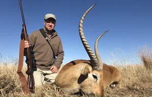 A hunter crouches down next to his red lechwe trophy.