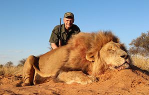 A hunter smiles with his lion trophy in the Kalahari.