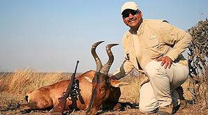 A hunter crouches proudly alongside his red hartebeest trophy.