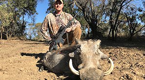 A hunter crouches down alongside his warthog trophy.
