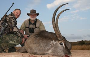 A pair of hunters smile with their waterbuck trophy.