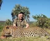 A hunter sits triumphantly alongside his leopard trophy.