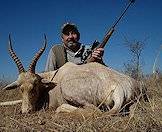 A hunter smiles triumphantly alongside his white blesbok trophy.