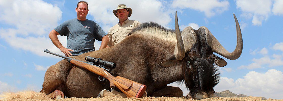 A hunter smiles proudly with his black wildebeest trophy and professional hunter.