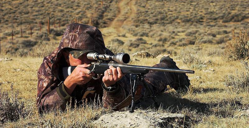 A hunter looks through his scope and prepares to fire his rifle.