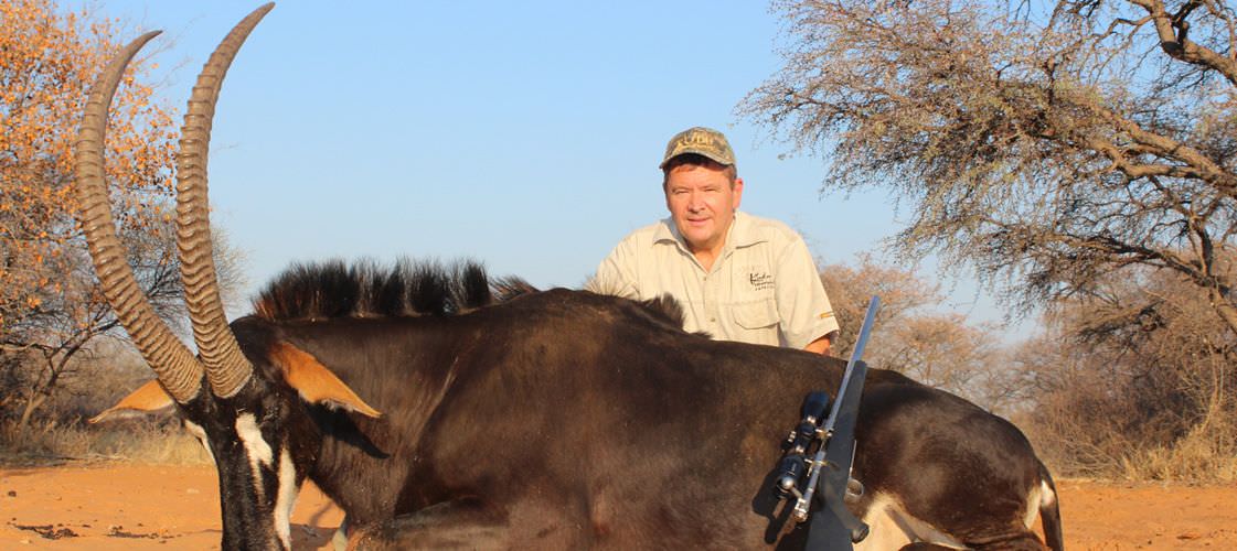 A hunter sits behind his impressive Sable antelope trophy.