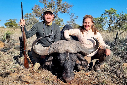 Hunters sitting next to a their buffalo trophy.
