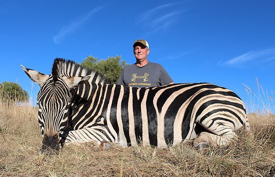 A hunter sits behind his zebra trophy.