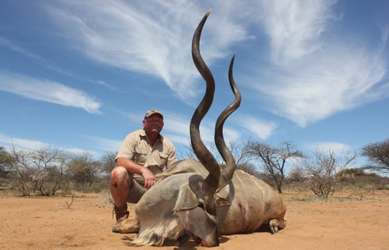 A hunter sits alongside an impressive kudu trophy.