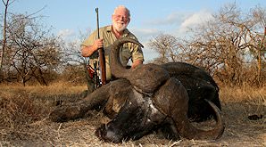 A proud hunter crouches down alongside his buffalo trophy.