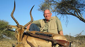 A hunter presents his rifle and impala trophy for a photograph.