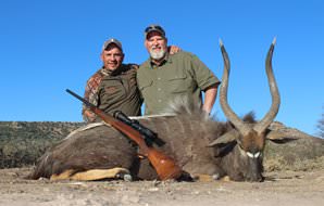A hunter smiles with his profesional hunter and nyala trophy.