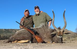 A hunter smiles with his profesional hunter and nyala trophy.