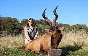 A red hartebeest trophy is propped up for a photo with a huntress.