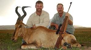 A hunter smiles with his red hartebeest trophy and professional hunter.