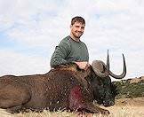 A hunter smiles proudly alongside his black wildebeest trophy.