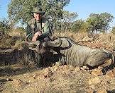 A hunter squats behind his blue wildebeest trophy.