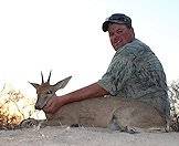 A hunter sits proudly alongside his grey duiker trophy.