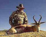 A hunter smiles proudly alongside his springbok trophy.