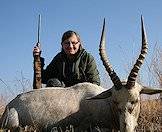 A huntress sits with her rifle and white blesbok trophy.
