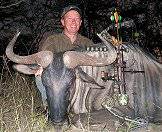 A close-up photograph of a bow hunter and his wildebeest trophy.
